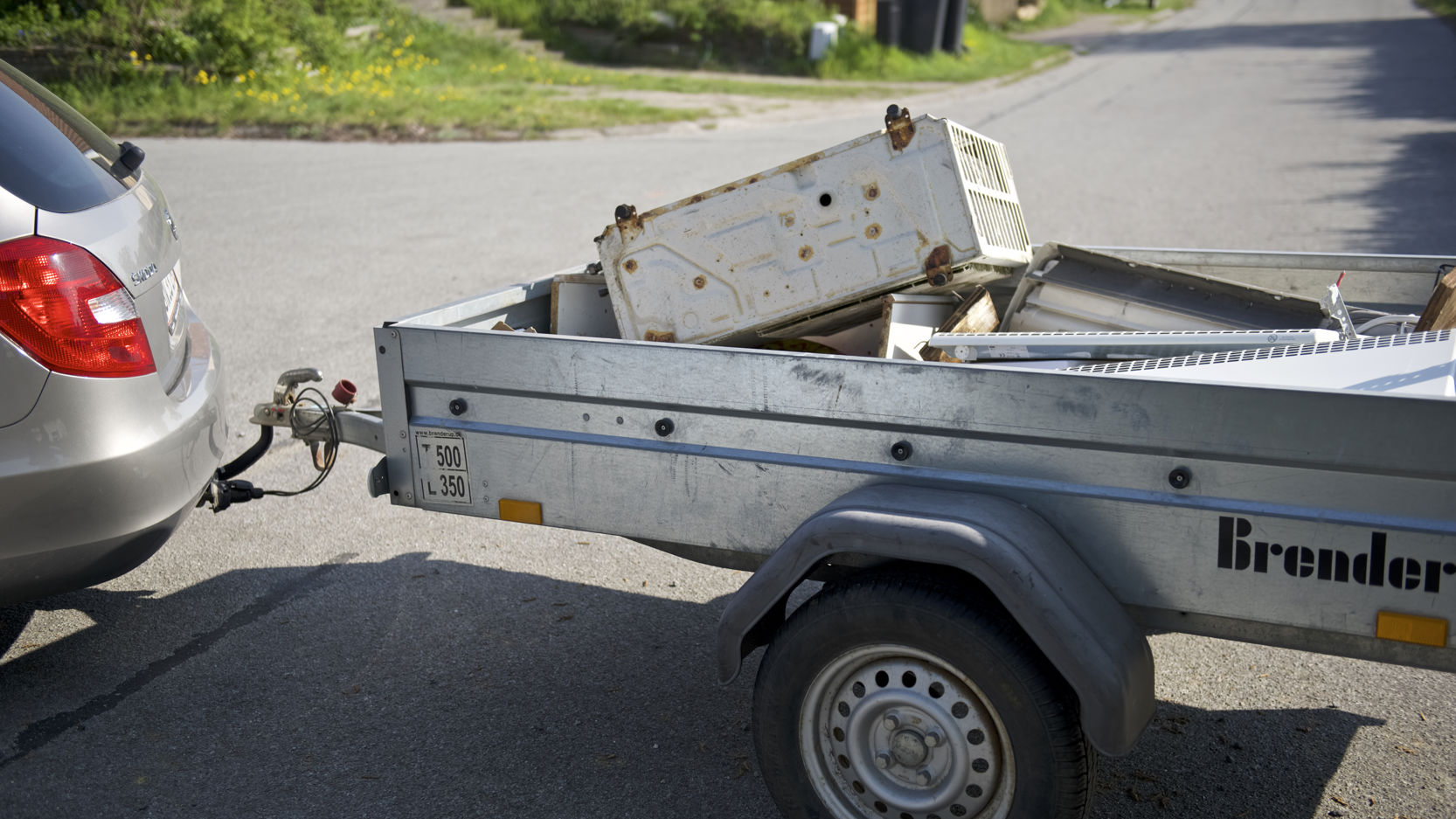 Trailer fyldt med gammelt elektronik og metaldele, tilkoblet en bil. Traileren er klar til at blive kørt til genbrugspladsen for korrekt affaldssortering og genbrug