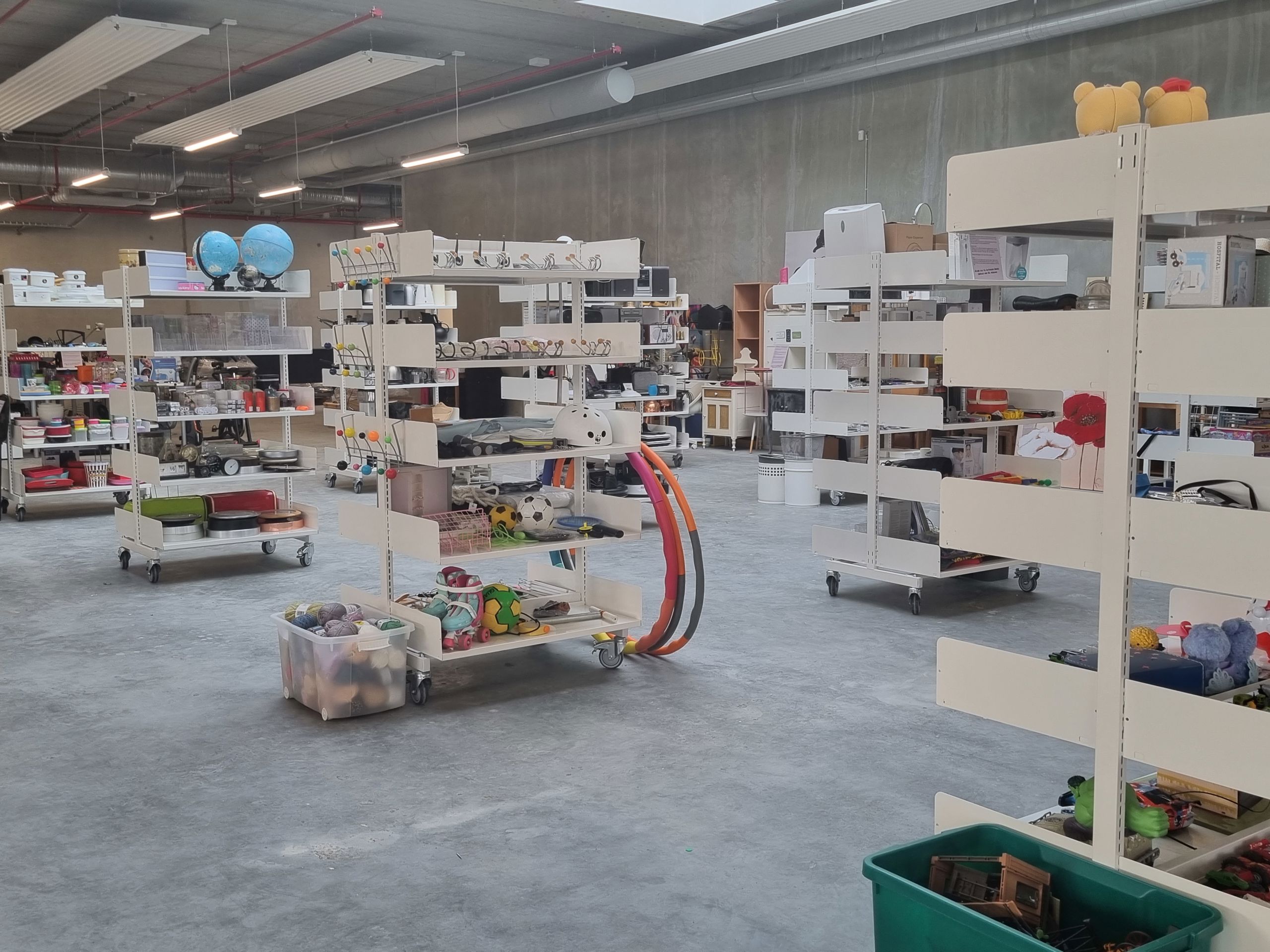 Foto af genbrugsbutikken på RessourceCenter Vejle. Rummet er fyldt med hylder, der indeholder forskellige genbrugsvarer som køkkenudstyr, legetøj, bøger og andre brugte effekter, der er gratis for borgere at tage med hjem