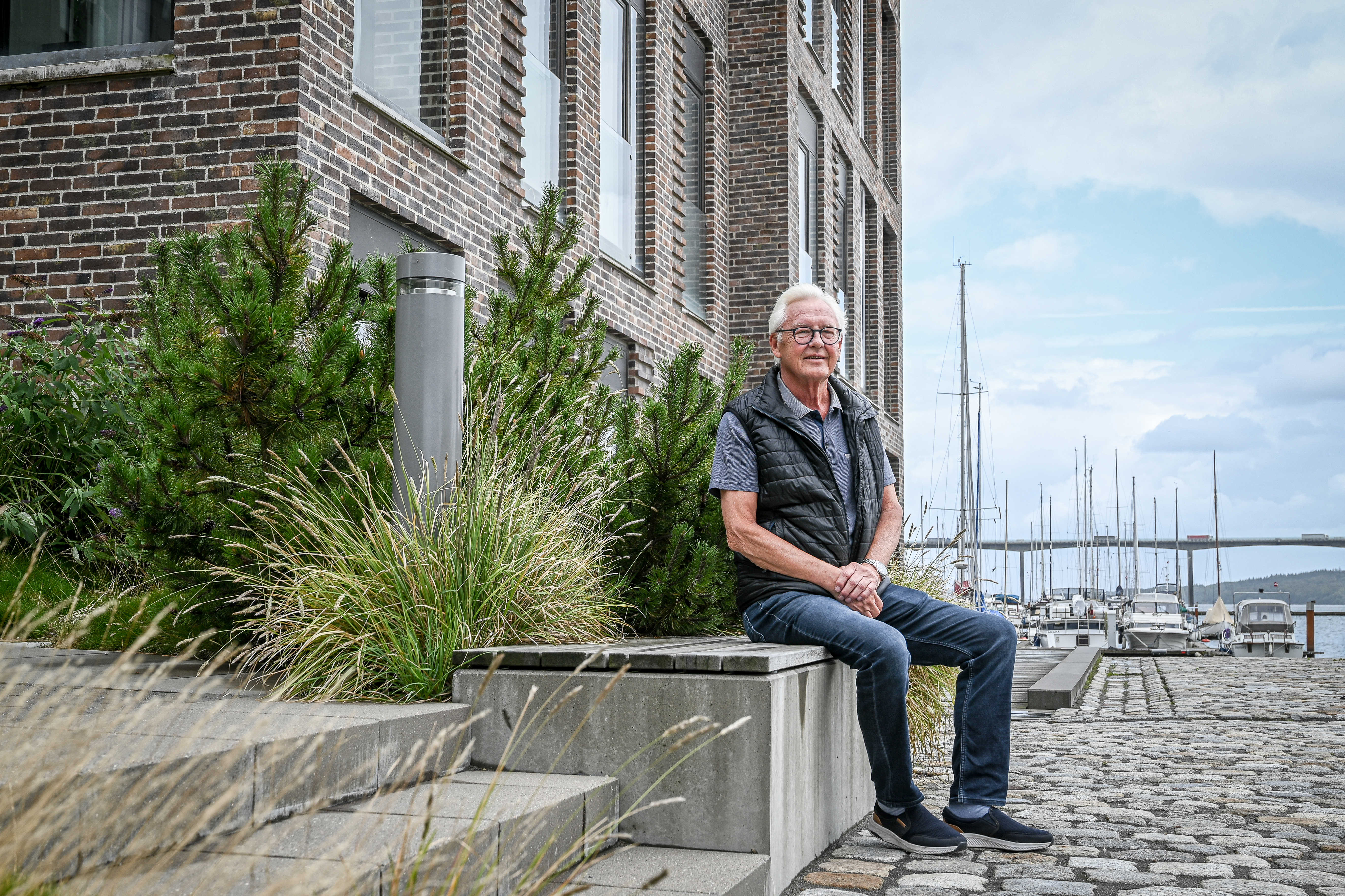 Leif sidder på en bænk foran boligområdet på Havneøen med lystbådehavnen i baggrunden.