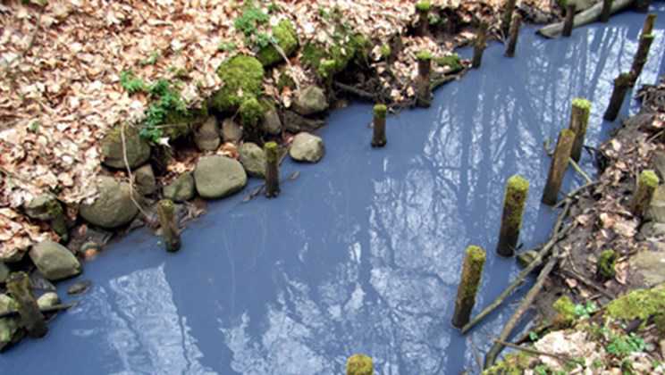 Blå maling hældt i en vejrist, som er endt i et vandløb.