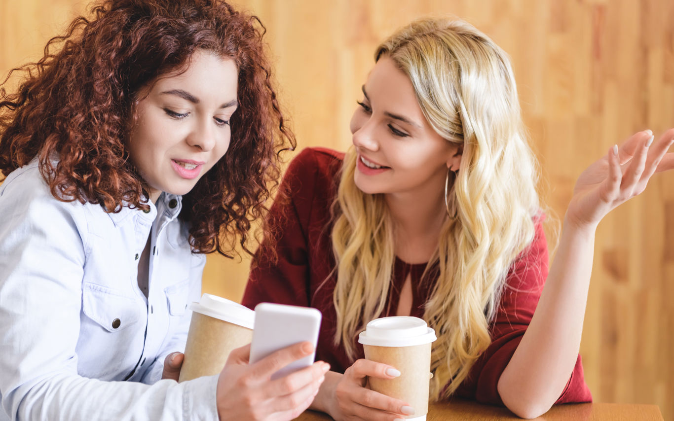 2 unge piger i samtale sidende med kaffekrus i hænderne