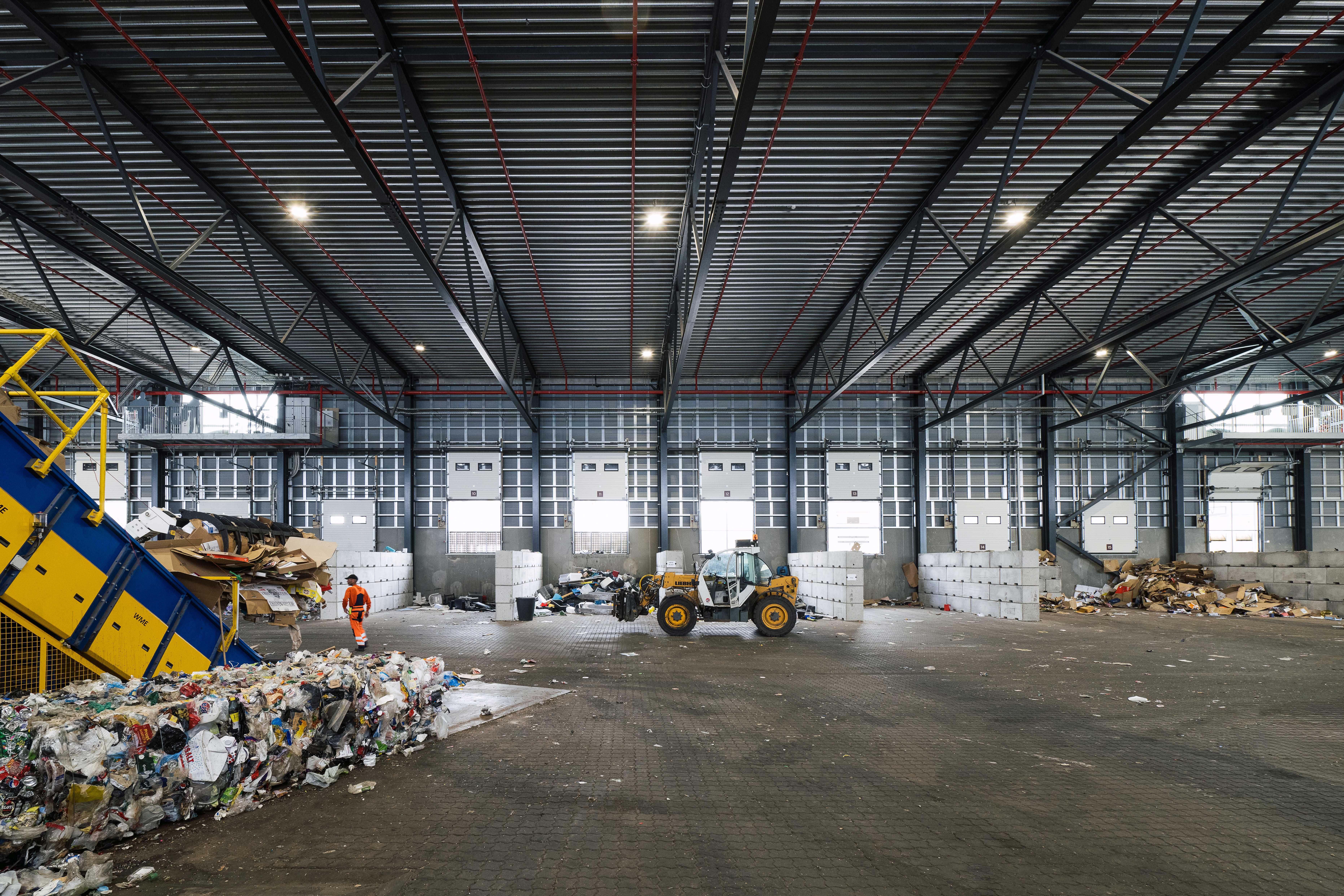 Indendørs foto af RessourceCenter Vejle's affaldssorteringshal med en gaffeltruck i arbejde og store bunker af sorteret affald, klar til videre forarbejdnin