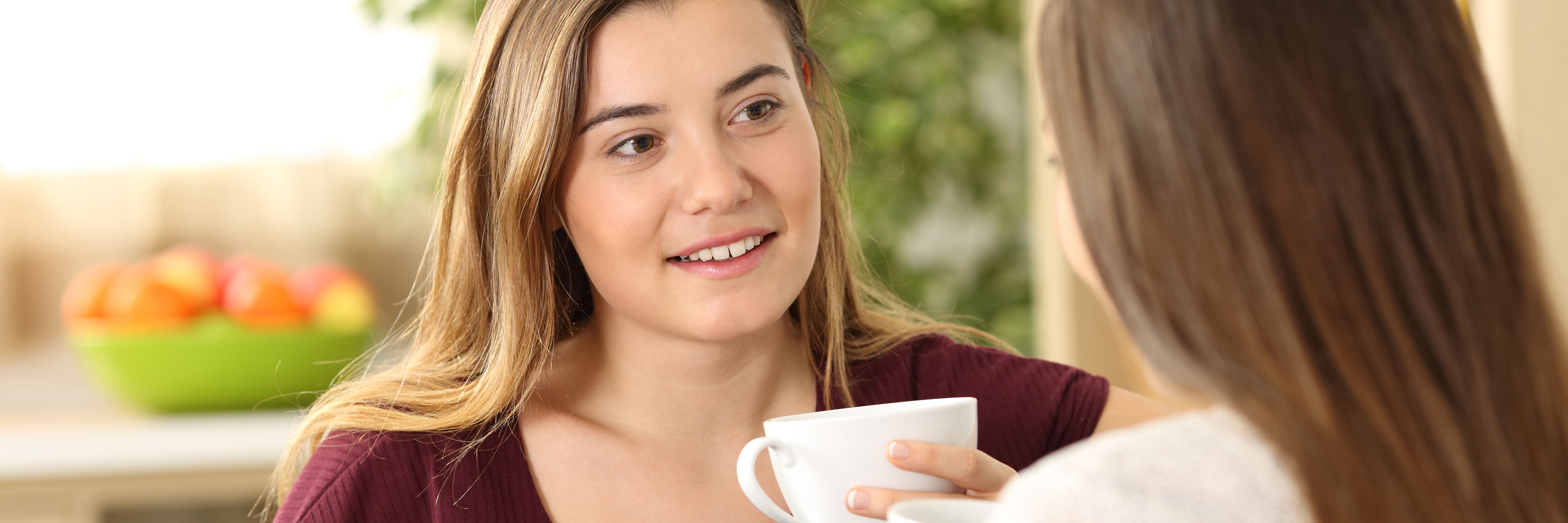 To piger i en samtale siddende tæt på hinanden med kaffekopper i hænderne