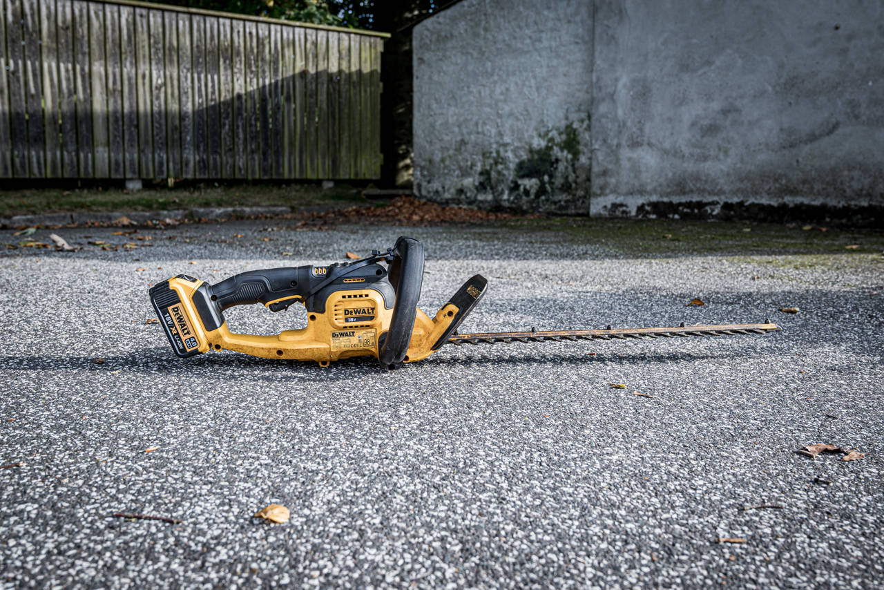 Hækkeklipper på jorden foran et plankeværk.
