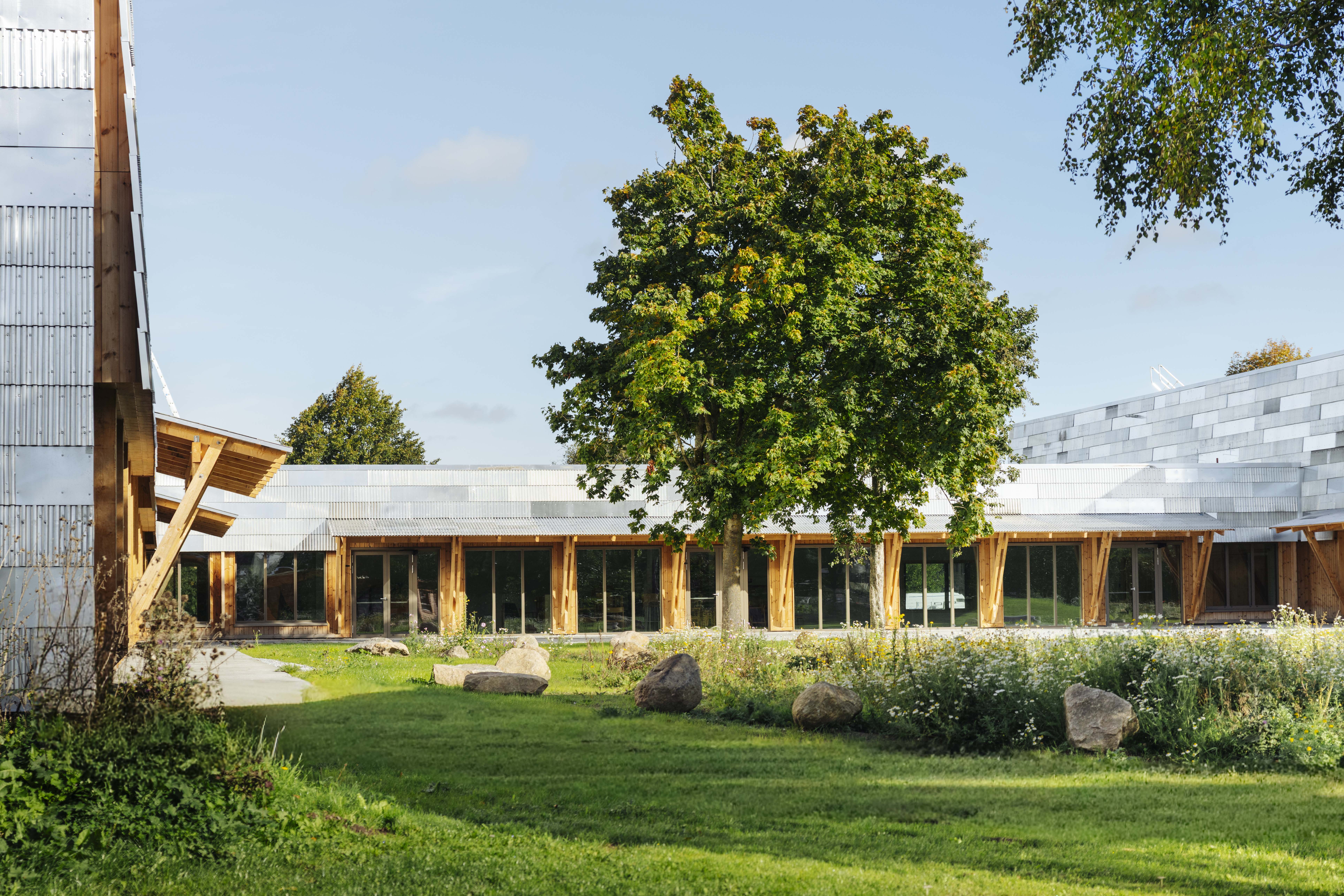 Foto viser ENGEN - Kulturhus & Bibliotek udefra. Der står et stort træ og masser grønt og blomster ude foran kulturhuset.