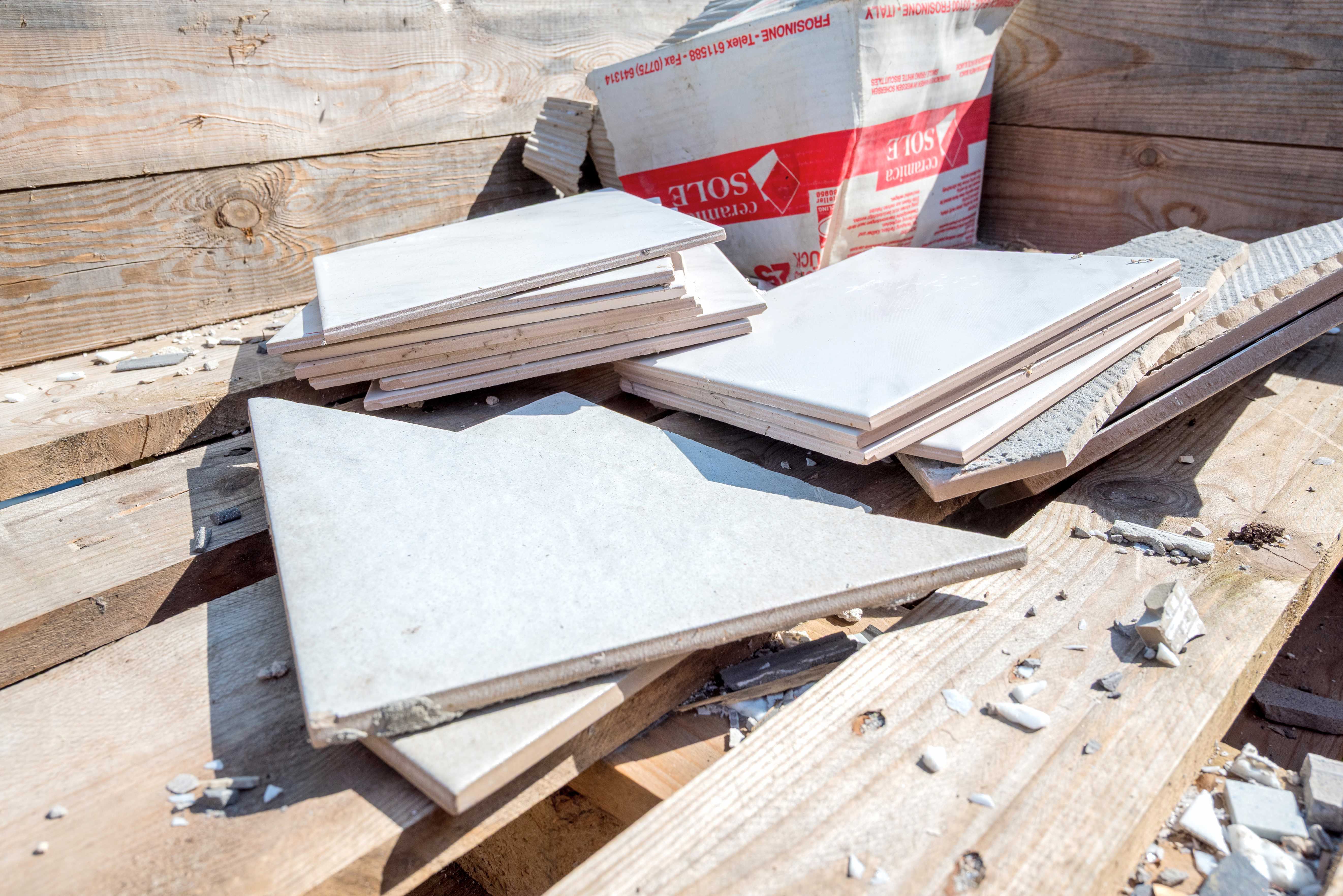 Brugte hvide og grå fliser stablet i en trækasse sammen med en sæk cement i BygIgen-afsnittet på Børkop genbrugsplads.