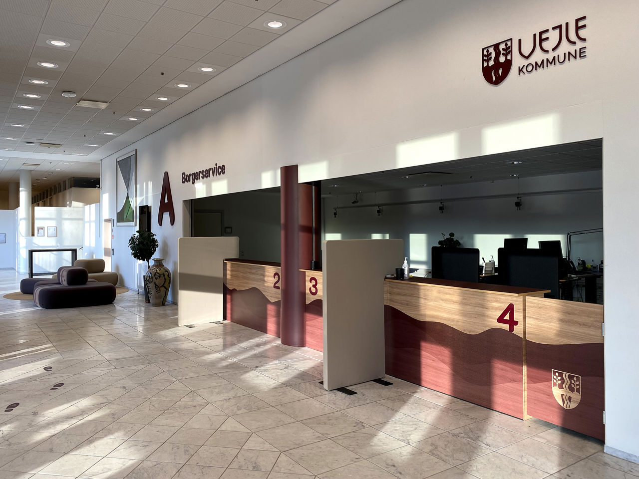 Receptionen i Borgerservice i Vejle Kommune med flere betjeningsskranker markeret med numrene 2, 3 og 4 samt skiltning på væggen, der viser kommunens logo.