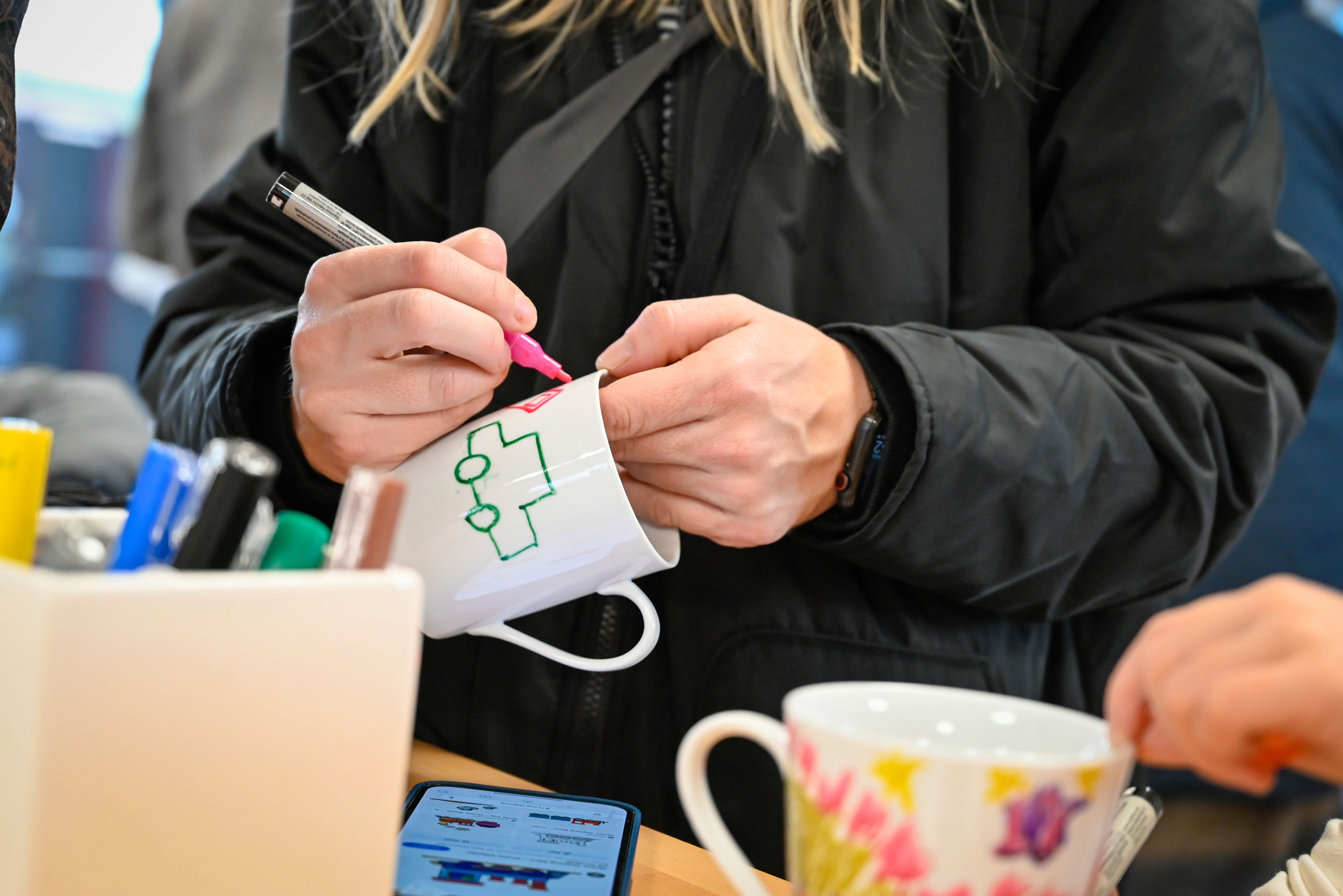 Person iført sort jakke maler med tusch på hvid kop af keramik.