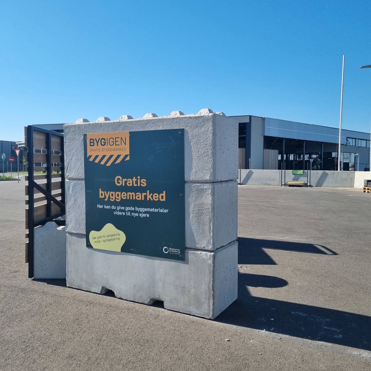 Skilt ved indgangen til BygIgen, et gratis byggemarked på RessourceCenter Vejle. Skiltet annoncerer "Gratis byggemarked" og inviterer borgere til at aflevere eller afhente gode byggematerialer, der kan genbruges.
