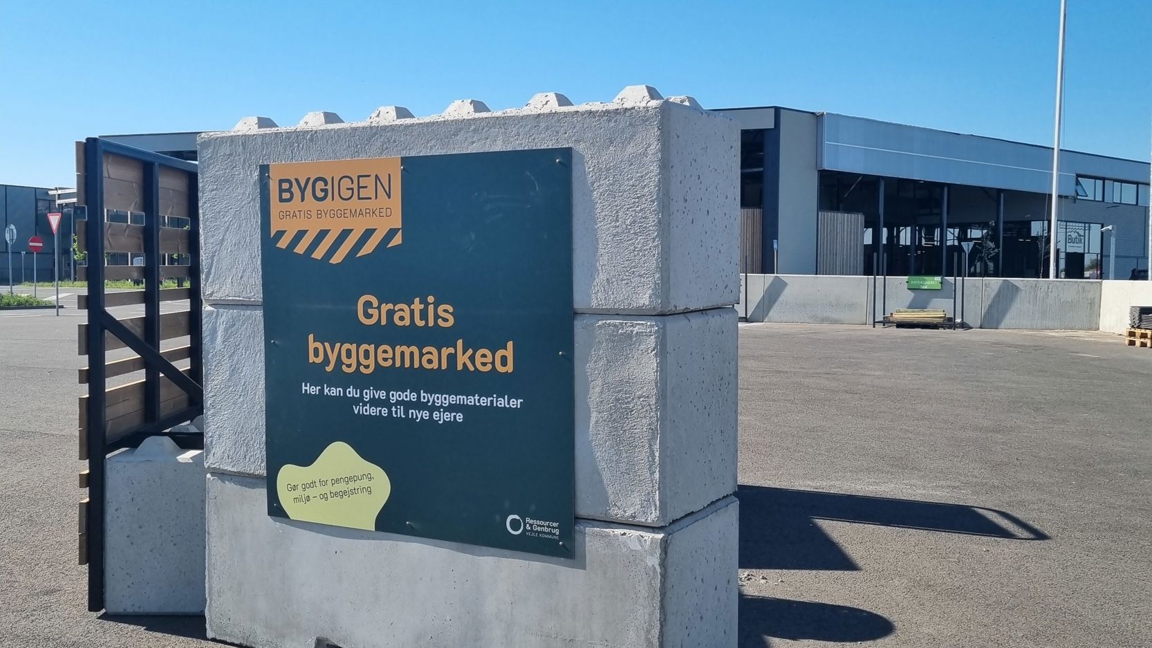 Skilt ved indgangen til BygIgen, et gratis byggemarked på RessourceCenter Vejle. Skiltet annoncerer "Gratis byggemarked" og inviterer borgere til at aflevere eller afhente gode byggematerialer, der kan genbruges.