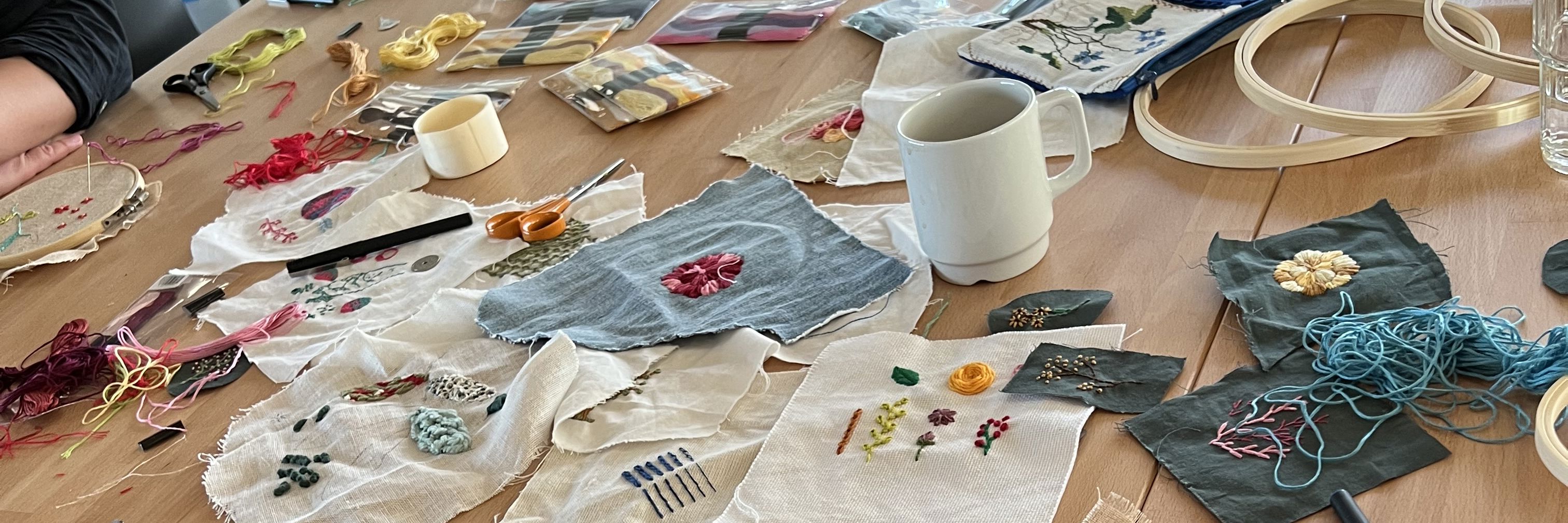 Workshop med broderi – bord fyldt med stofstykker, tråd og håndarbejde i gang.