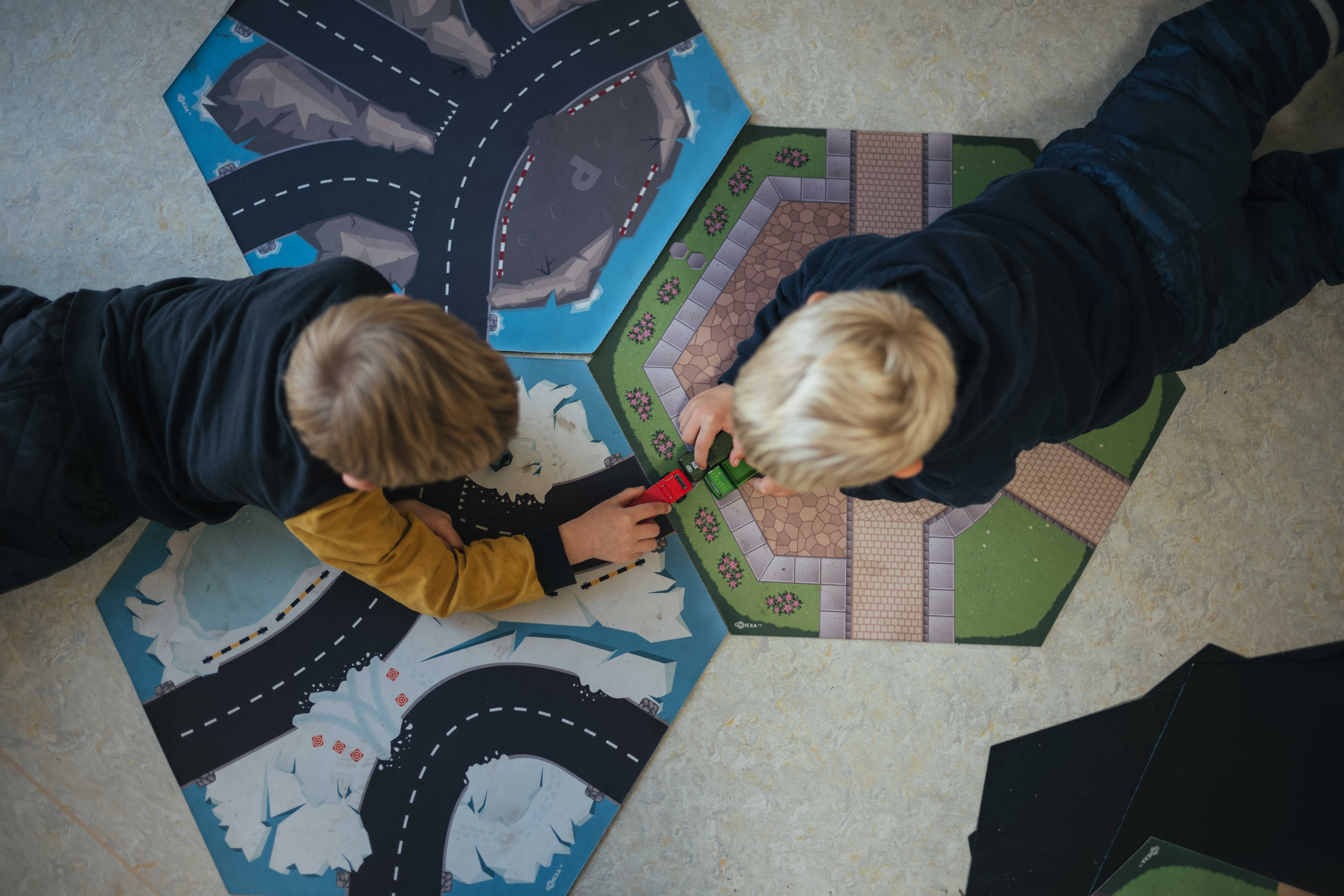 To drenge ligger på gulvet og leger med biler på tre små tæpper med veje