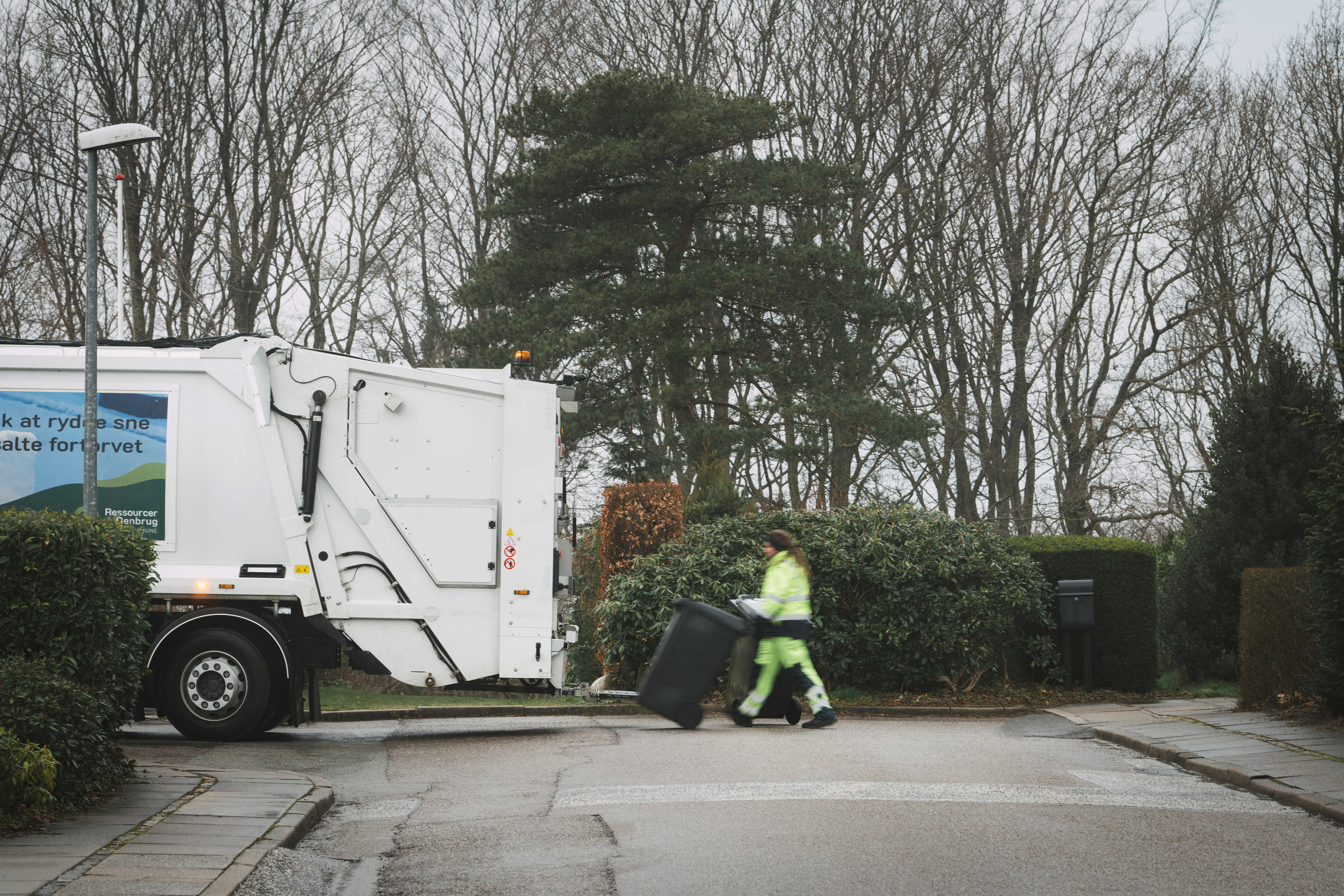 Skraldemand trækker en affaldsbeholder over vejen til skraldebilen på en stille villavej