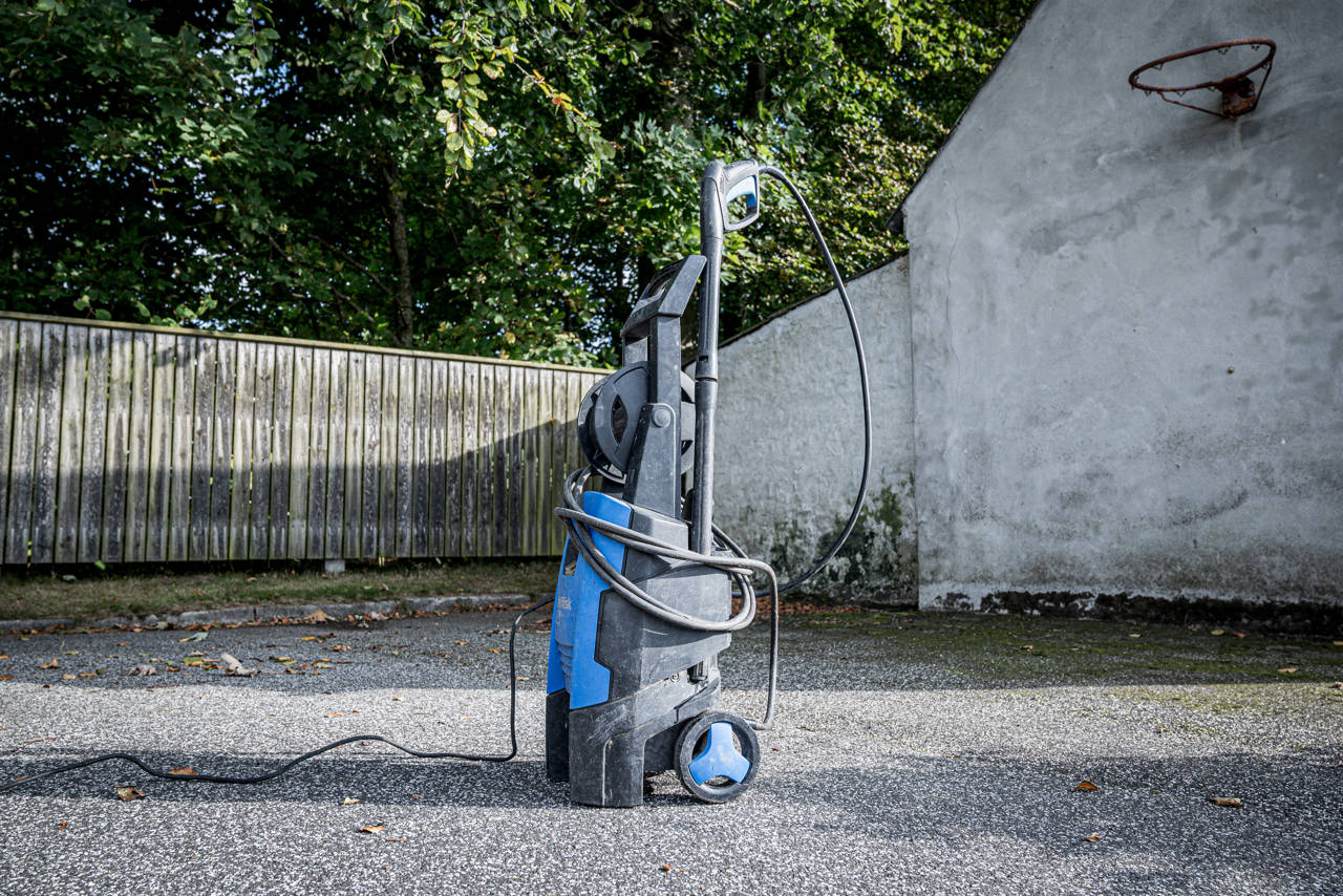 Højtryksrenser placeret på asfalt foran et plankeværk.