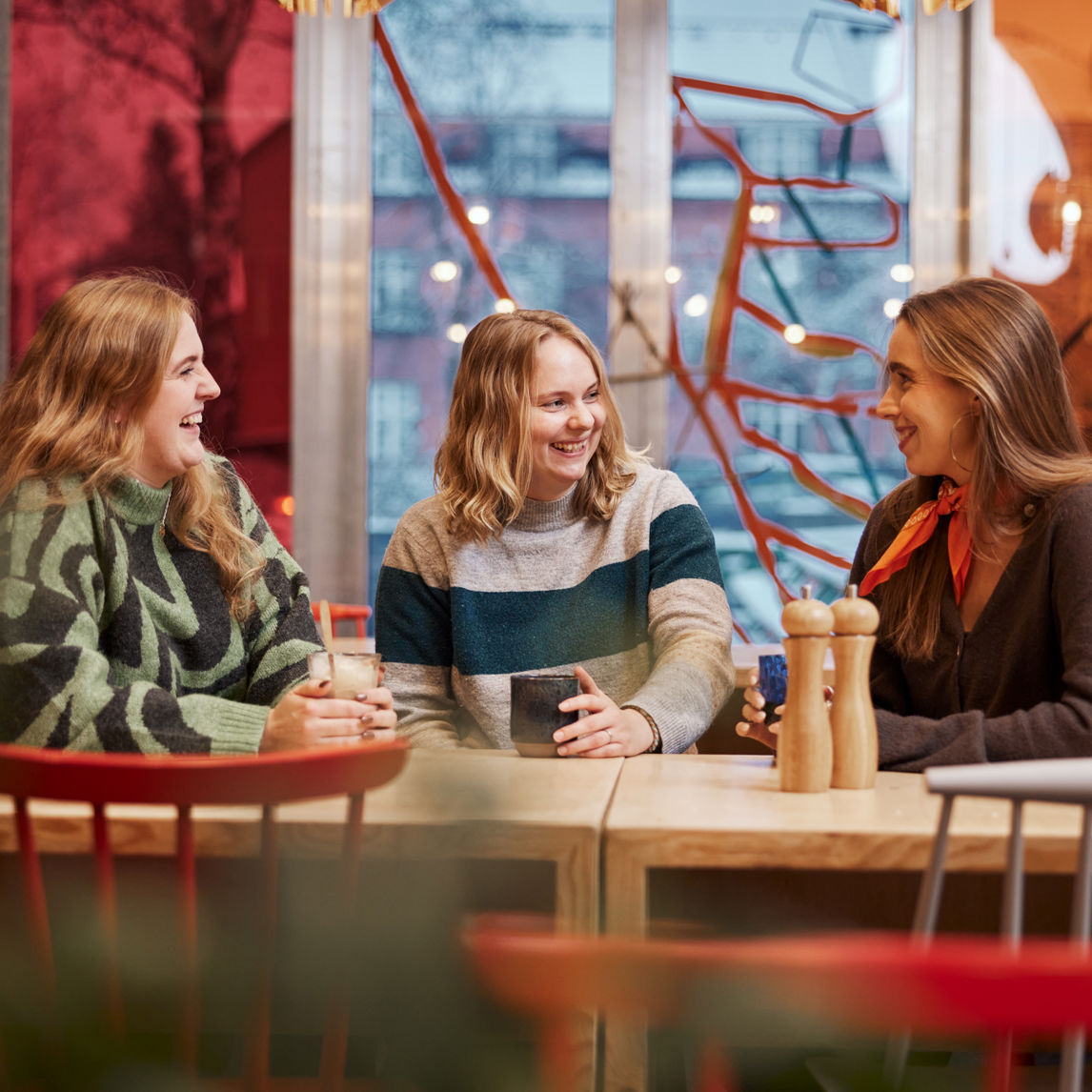 Foto af unge siddende ved et bord med kaffe/the i hænderne