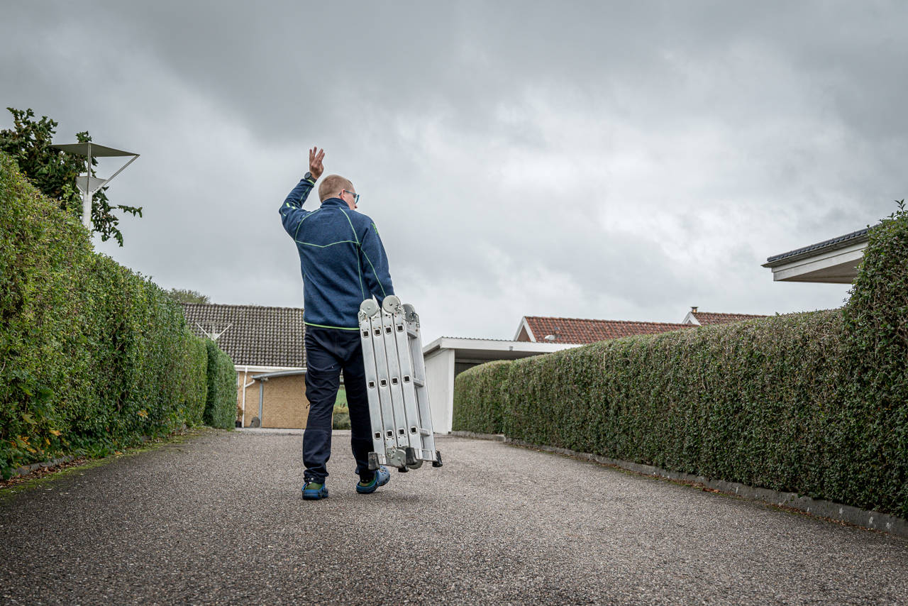 Rasmus vinker til en nabo over hækken, idet han går ned til fællesskuret for at returnere den stige, han har lånt.