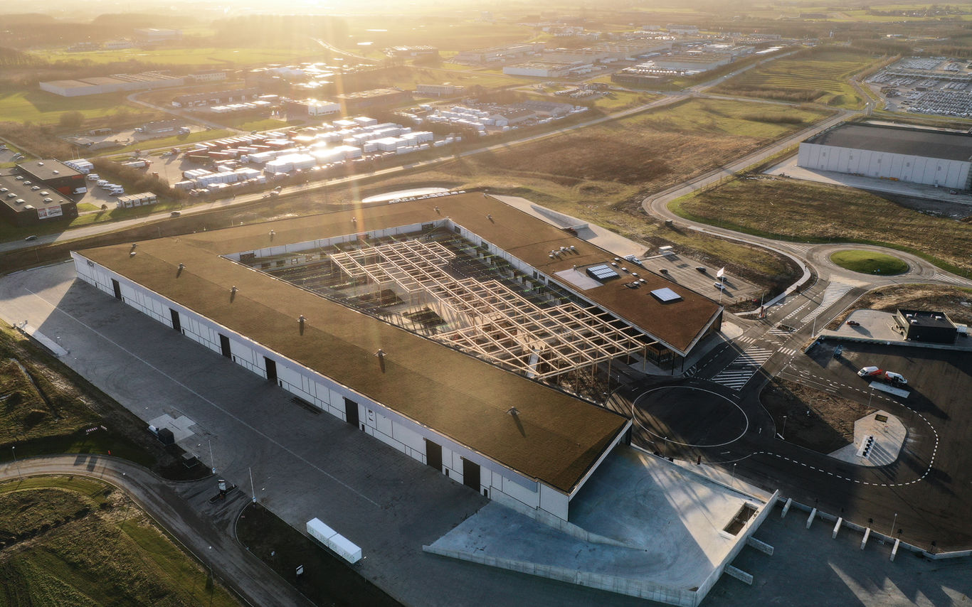 Dronefoto af RessourceCenter Vejle (RCV) med et grønt tag og solpaneler, omgivet af parkeringsplads og grønne områder, der viser centerets bæredygtige arkitektur og indre gårdstruktur.