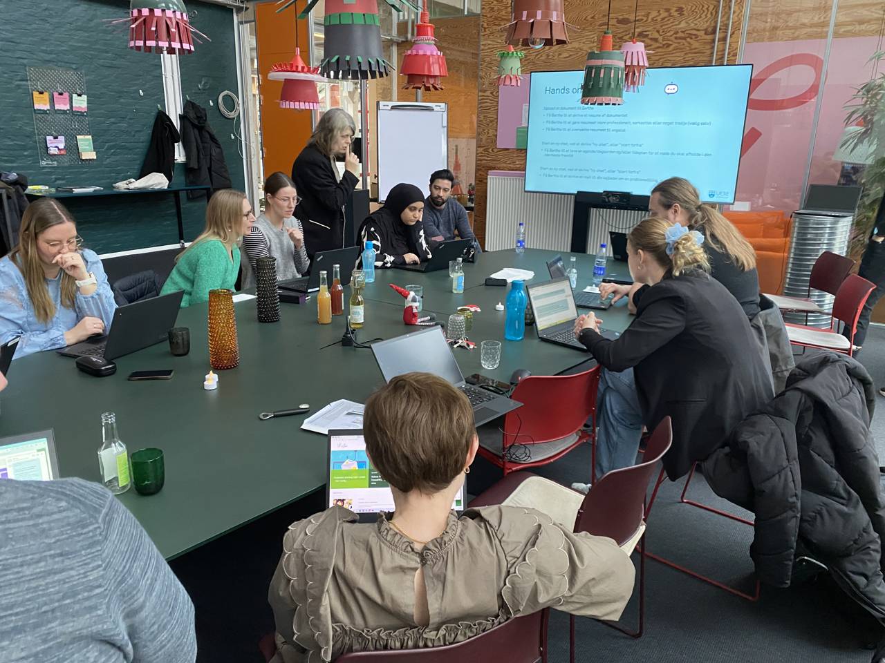 Stemningsbillede - man ser 9 elever på et kursus - sidder omkring mødebord og arbejder koncentreret med kunstig intelligens på pc