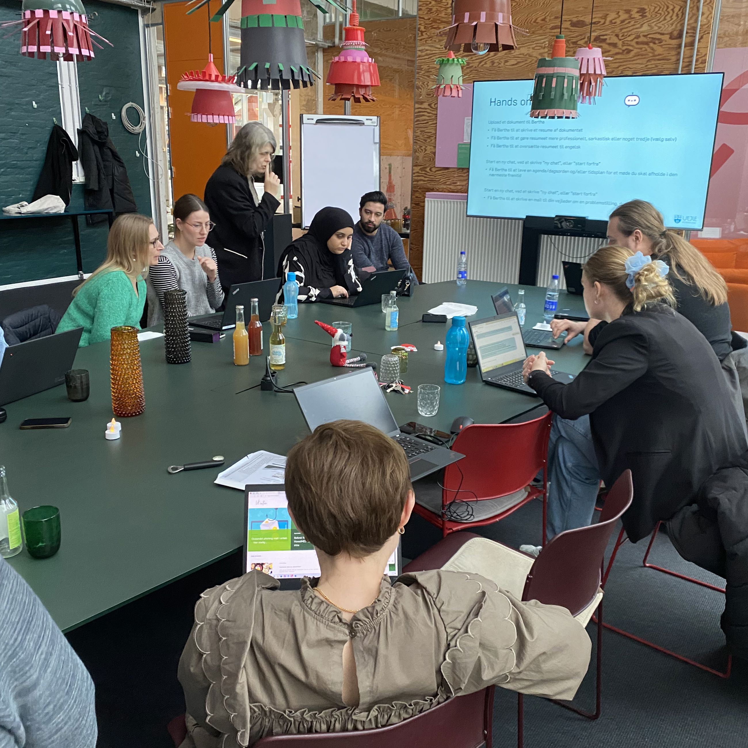 Stemningsbillede - man ser 9 elever på et kursus - sidder omkring mødebord og arbejder koncentreret med kunstig intelligens på pc