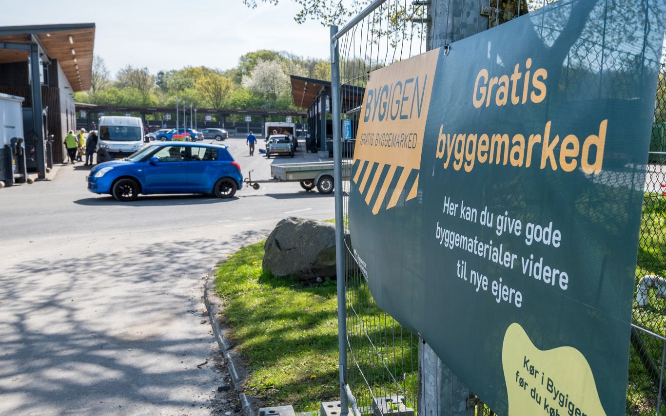 Skilt ved indgangen til BygIgen ved Børkop Genbrugsplads. Skiltet annoncerer "Gratis byggemarked" og inviterer borgere til at aflevere eller afhente gode byggematerialer, der kan genbruges.