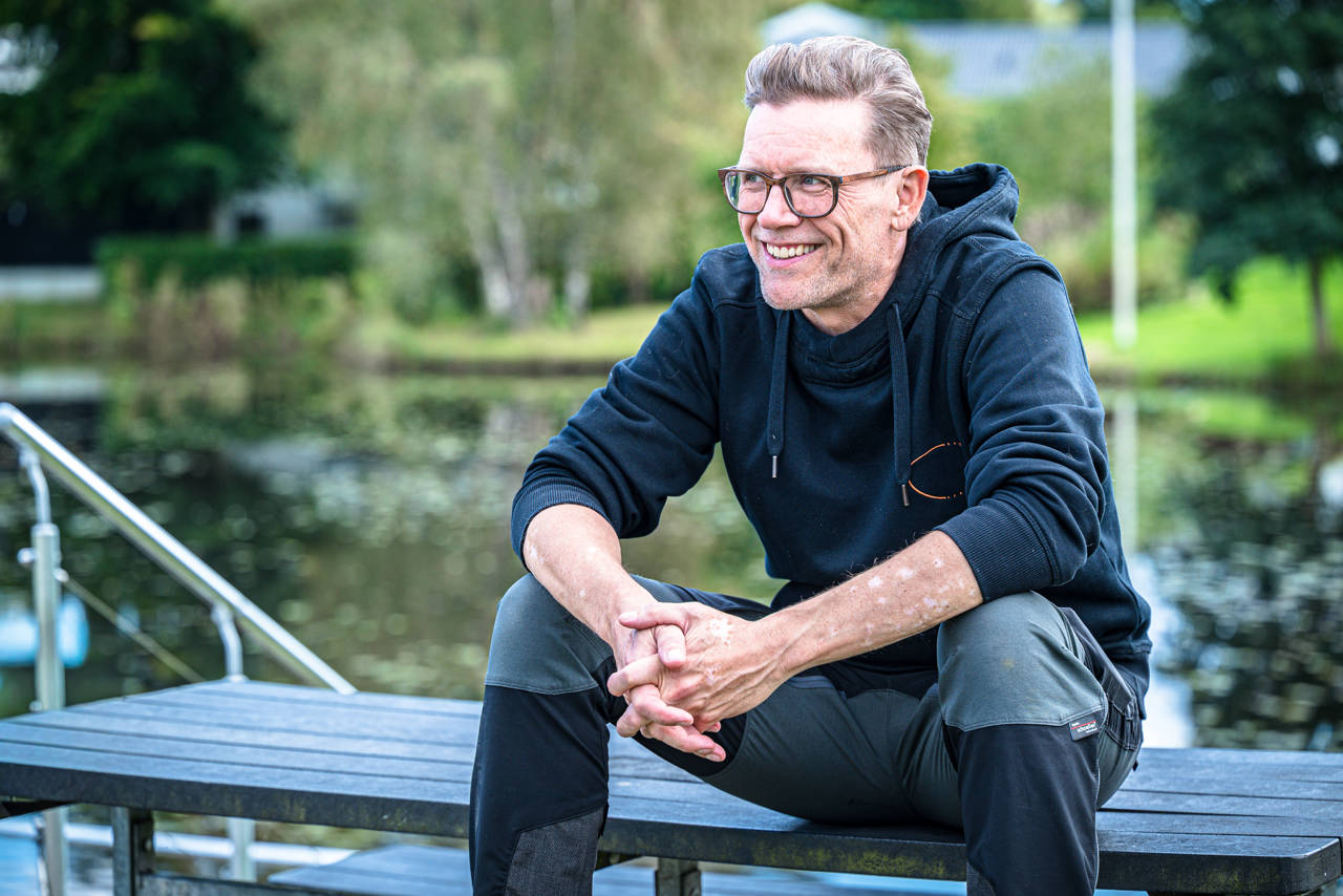 Tomas sidder på en træbænk ved Uhrhøj Sø og smiler.