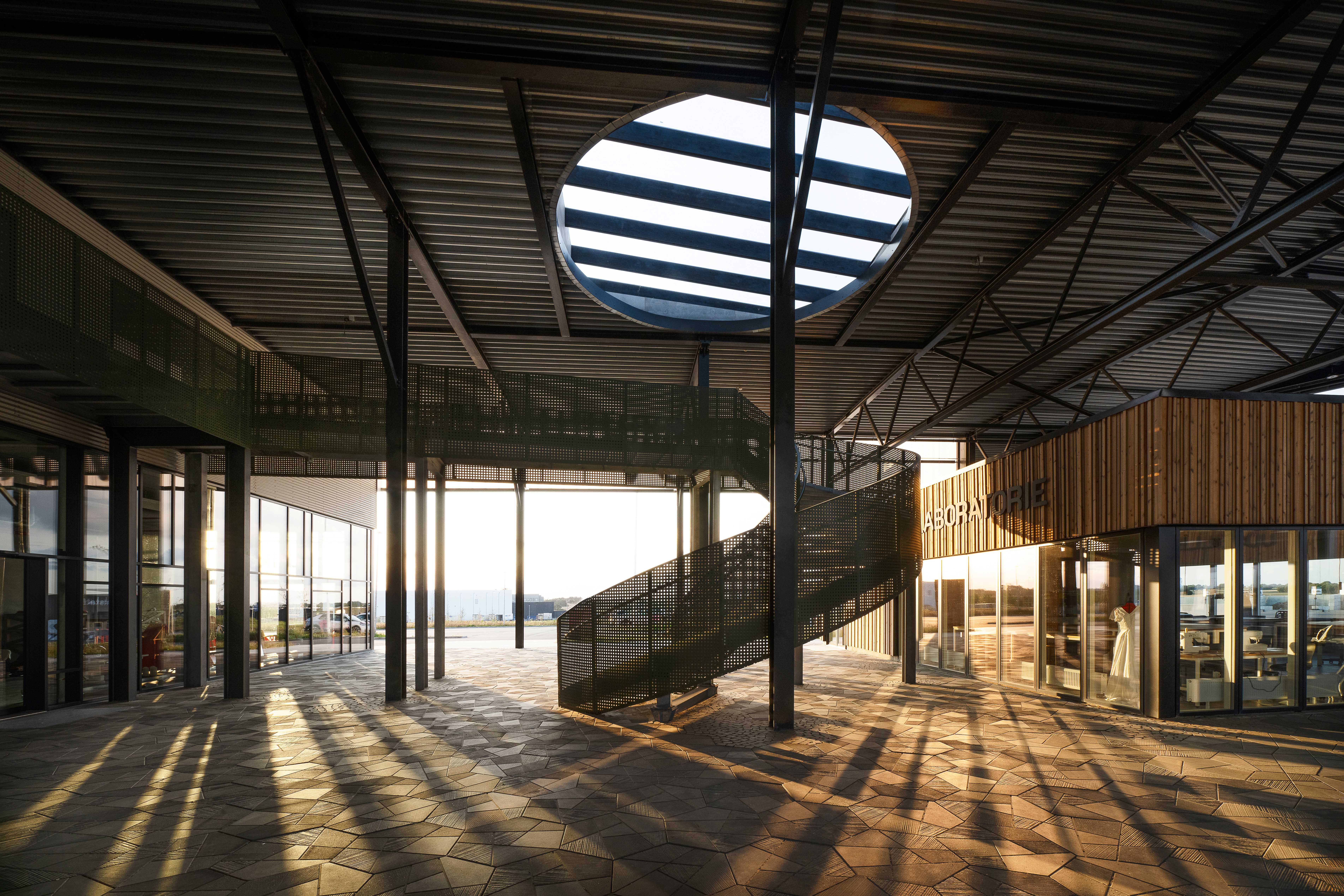 Interiørbillede af RessourceCenter Vejle med moderne arkitektur, cirkulært ovenlysvindue og en spiraltrappe, badet i aftensolens varme lys