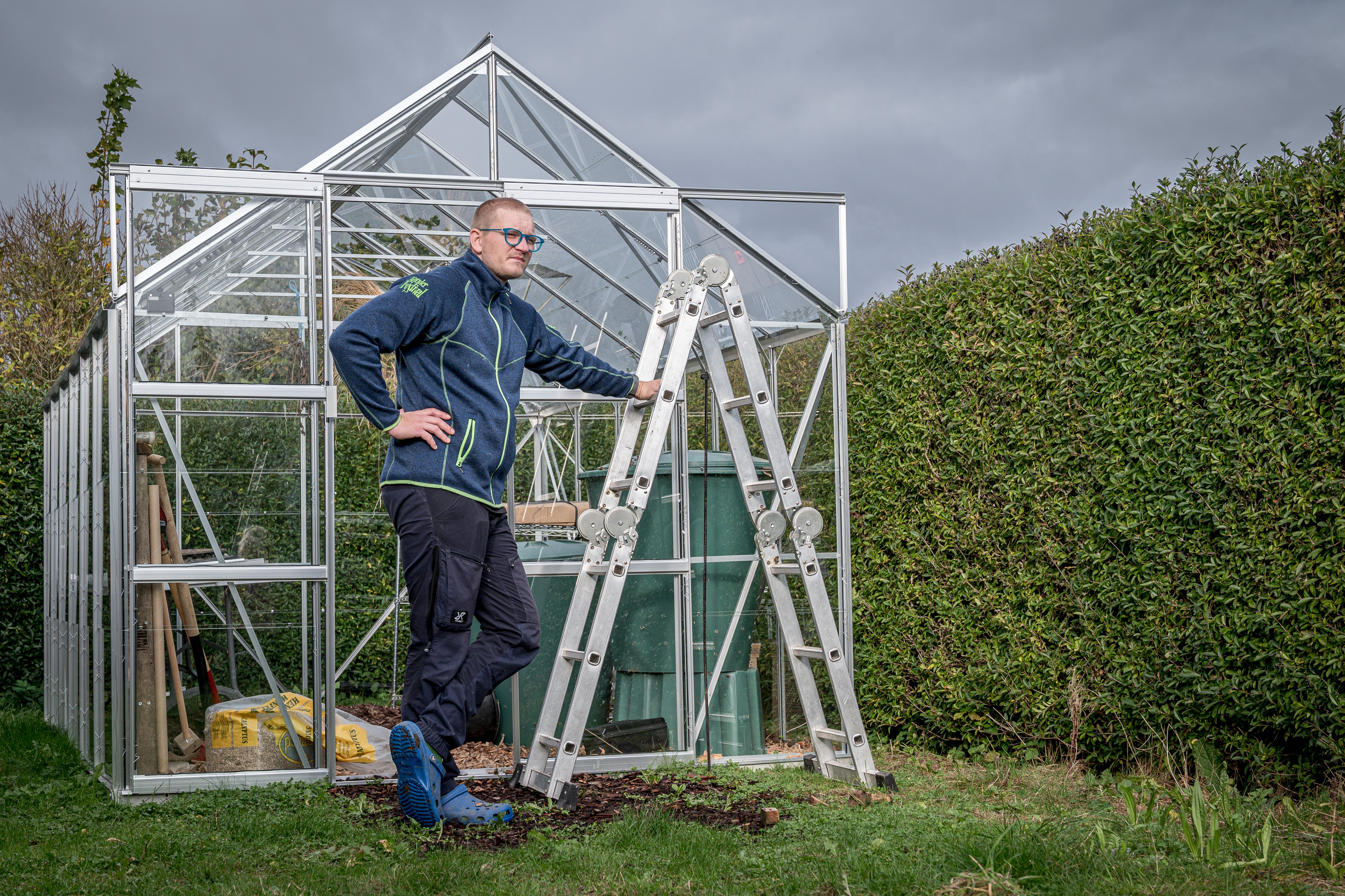 Rasmus med stigen fra fællesskuret foran sit drivhus.